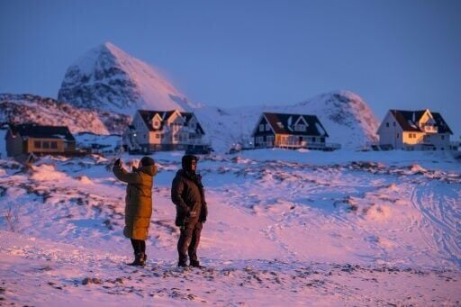 Locals stand on a snowy shoreline at dusk in Nuuk, Greenland