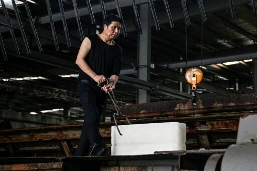 A worker uses tongs to move ice blocks inside a refrigerated store at the Feichao Ice Factory in Hangzhou. Heatwaves across China have caused demand for ice to soar