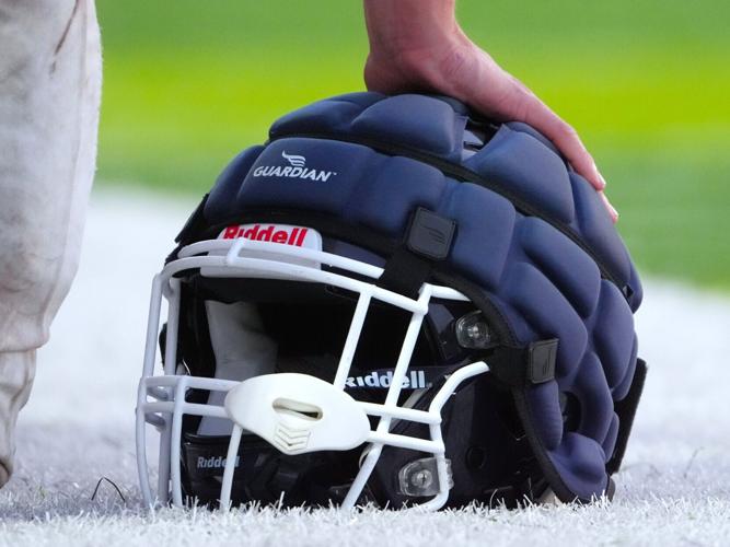 A football player puts his hand on his helmet with a Guardian cap on the sidelines during a high school scrimmage at Norton High School in Norton, MA on Sept. 4, 2026.