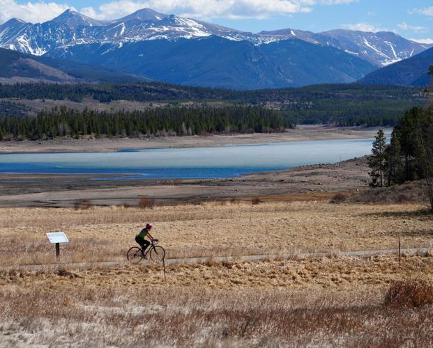 A person rides their bike in front of Lake Dillon in Frisco, Colorado, on March 26, 2026, as the reservoir sits at a low level before spring snowmelt begins refilling it. Water managers fear the poor snowfall this winter means the lake will receive far les