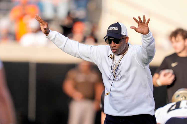 Colorado coach Deion Sanders stands on the field as the team warms up before a college football game between the Oklahoma State