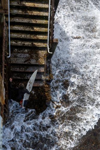 A surfer makes her exit from the beach during high tide at a closed beach access stairway in Encinitas
