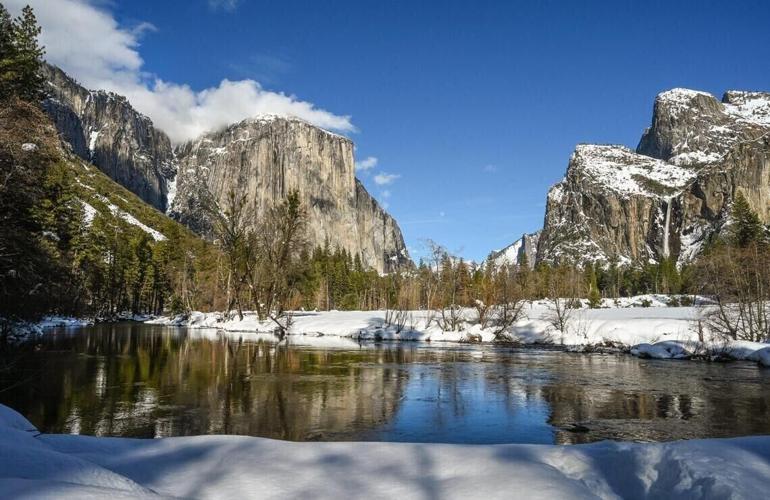 Clouds graze the top of El Capitan, left, as Bridalveil Fall, right, flows down into Yosemite Valley and the Merced River while a heavy blanket of snow covers the roadway banks on March 3, 2023.