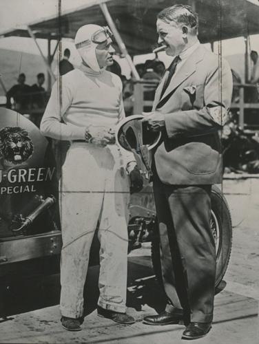(From left) Three time Indy 500 winner, Wilber Shaw holds an early racing helmet while chatting with Barney Oldfield “The Speed King,” at the Legion Ascot Speedway in California. Shaw used his experience working at Firestone to help develop synthetic ru...
