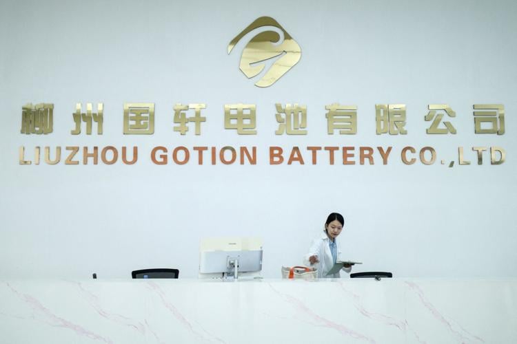 A woman stands next to a logo of Chinese battery maker Gotion, in Liuzhou