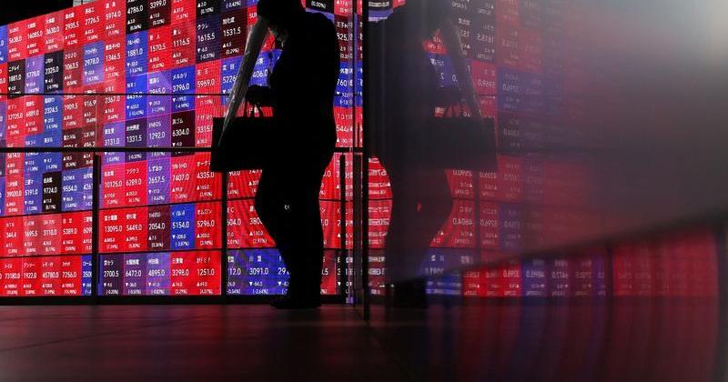 A man walks in front of an electronic screen displaying Japan's Nikkei stock prices quotation board inside a conference hall in Tokyo