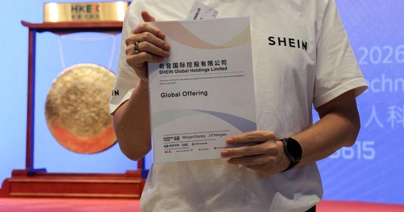 A staff member holds a prospectus and poses for photos during the listing ceremony of online retailer Shein at the Hong Kong Stock Exchange, in Hong Kong