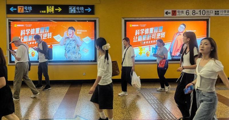 People walk past billboards from Innovent Biologics and Meituan displayed in a metro station in Shanghai