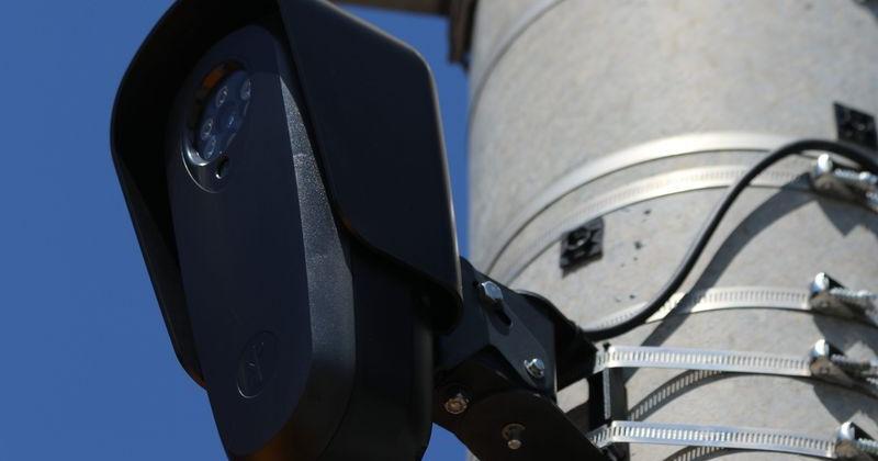 This Flock camera, at the intersection of Broadway and Exchange Street in Pawtucket, Rhode Island, is mounted on a metal utility pole, nestled amid street signs and crosswalk signals.