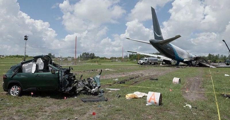 A damaged car sits next to the wreckage of an Amazon Prime Air cargo plane after it overran a runway at Miami International Airport.