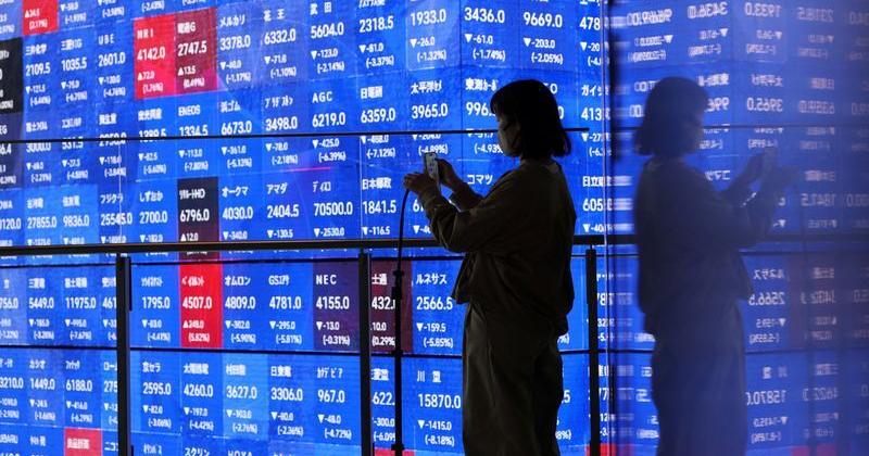 A visitor stands next to an electronic screen displaying Japan's Nikkei stock prices quotation board inside a conference hall in Tokyo