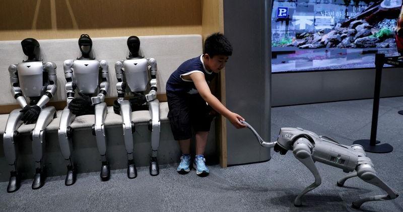 Child sits next to Unitree's G1 humanoid robots as he interacts with a Unitree's GO2 robot, at a Unitree store in Beijing