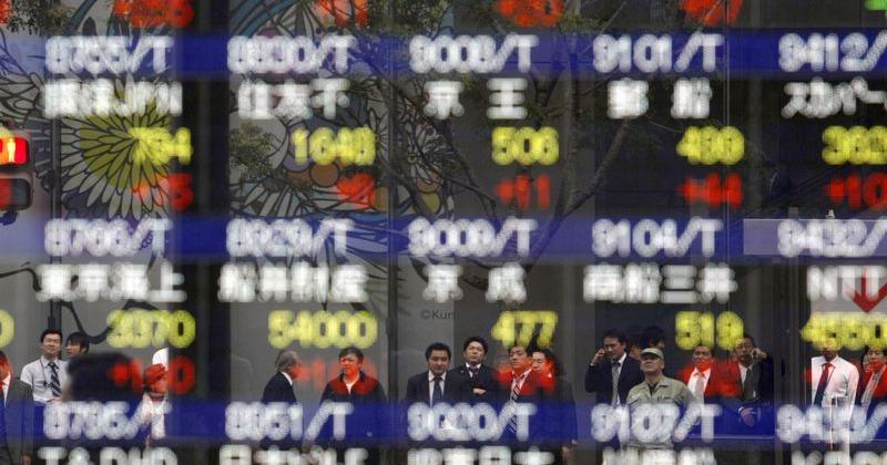 People are reflected in a stock index board outside a brokerage in Tokyo