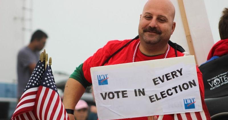 A man holds up a League of Women Voters sign encouraging voting during the Barefoot Mardi Gras parade Feb. 10, 2018. The League of Women Voters is a nonpartisan organization that supports election participation.
