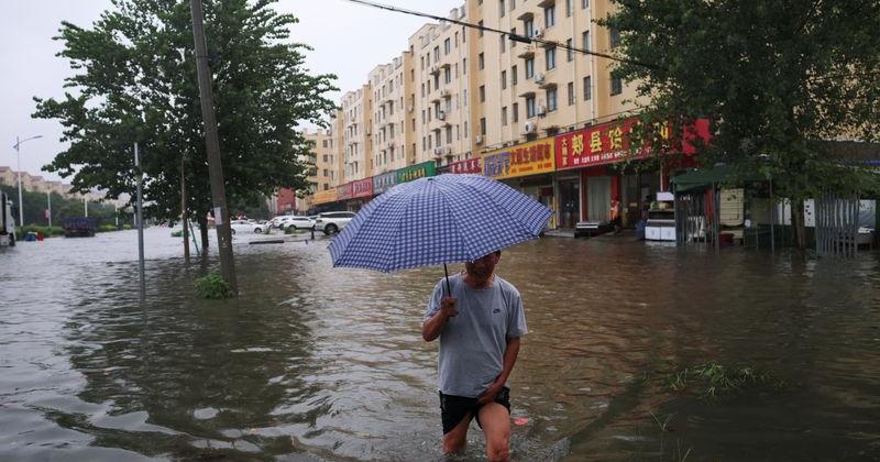 Man holds an umbrella as he wades through floodwaters on a street, amid heavy rainfall brought by remnants of Typhoon Dolphin, in Luohe