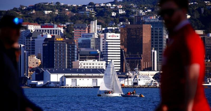 Pedestrians walk past a sailing boat as it passes in front of the central business district of Wellington in New Zealand