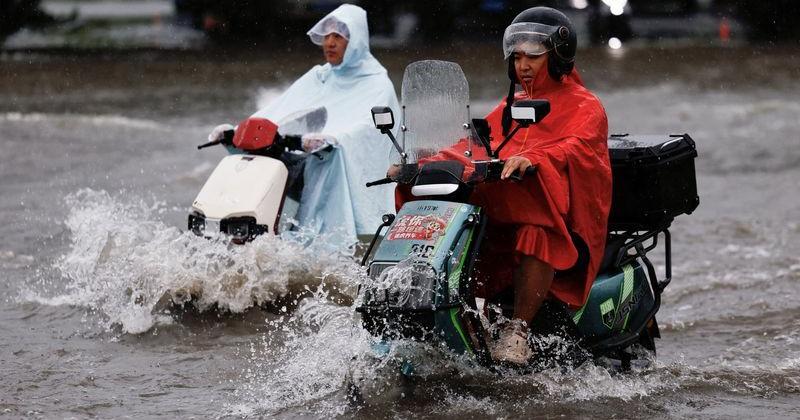 People ride on scooters as they travel through waters on a flooded street, amid heavy rainfall brought by remnants of Typhoon Dolphin, in Zhengzhou