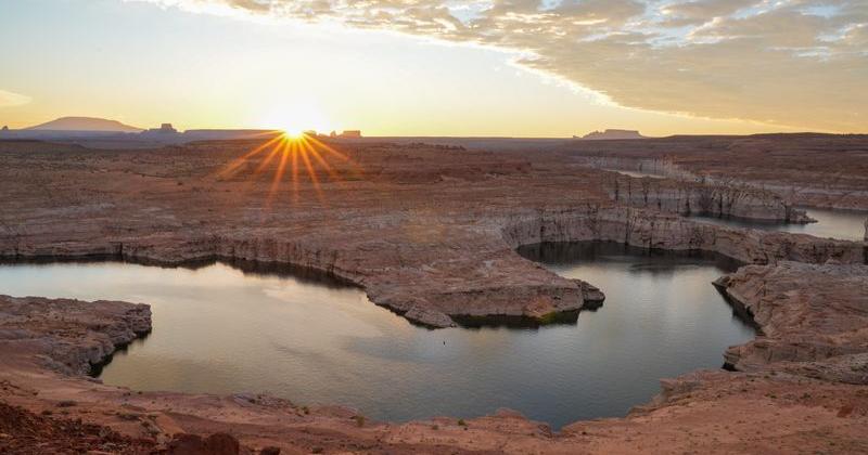 The sun rises above the horizon near the sacred Navajo Mountain, left, to reveal Lake Powell and the Glen Canyon near Page, Arizona, on Oct. 6, 2026.