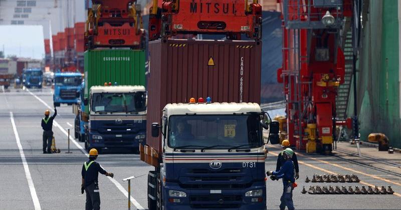 Workers load containers onto a cargo ship at an industrial port in Tokyo