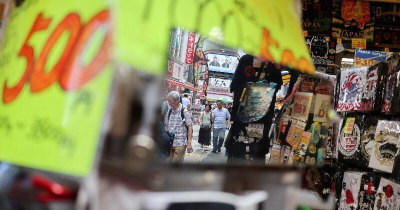 Shoppers and passersby are reflected in a mirror in front of a retail store in Tokyo