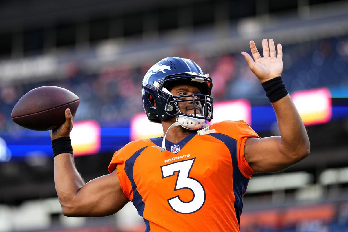 Retired NFL quarterback Peyton Manning, back, waits to take a swing in the  batting cage as Denver Broncos quarterback Russell Wilson, front right,  confers with Vinny Castilla, special assistant to the general