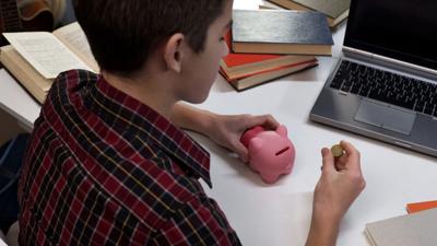 Teen in classroom examines coin, holds piggy bank