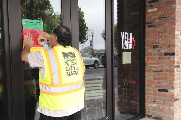 A city employee taping up an unsafe sign on a building after the Napa earthquake