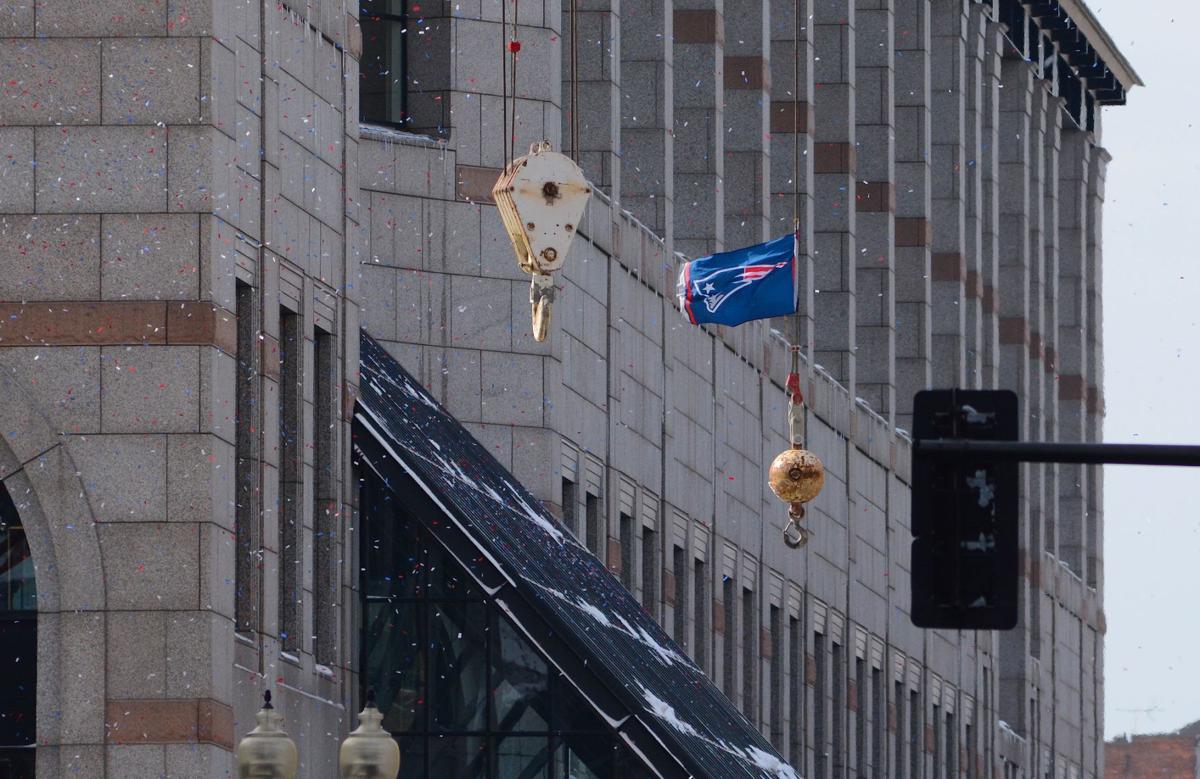 As a confetti cannon launches red, white and blue paper into the air above Boylston Street, construction crews working on the Prudential Center hoist a New England Patriots flag above the street as the parade to celebrate the team's Super Bowl win begins.