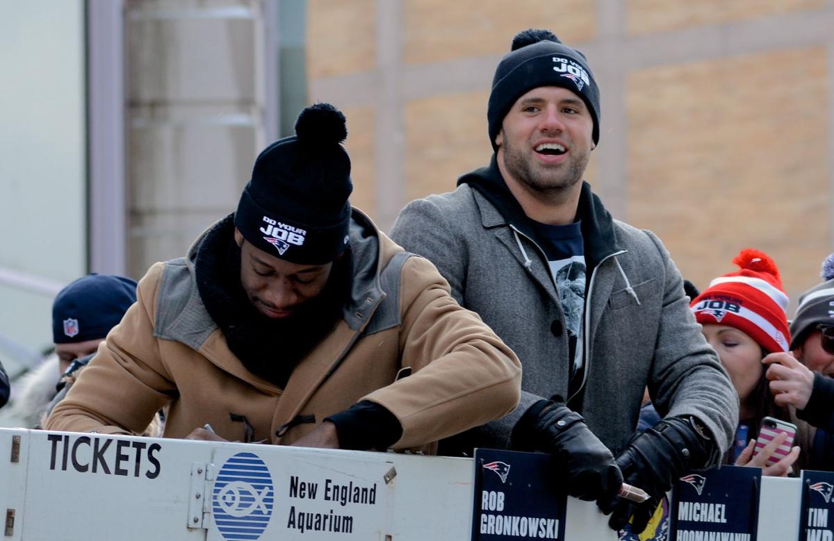 Patriots Fullback James Develin, right, looks out at the crowd from the top of a Duck Boat as tight end Tim Wright, left, signs an autograph during the team's celebratory parade.