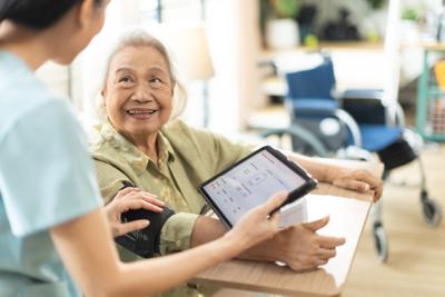 Woman asian nurse taking blood pressure of a senior woman patient at home.Home care healthcare professional using digital tablet