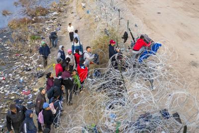 Immigrants try to pass over razor wire after crossing the border into El Paso, Texas from Ciudad Juarez, Mexico.