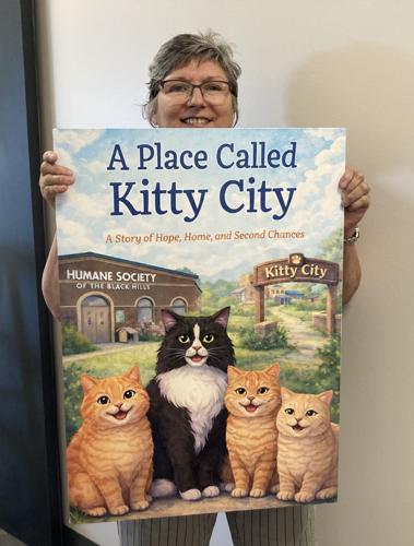 Tammy Barrows, executive director of Humane Society of the Black Hills, holds a poster-sized image of a new book that celebrates Kitty City. Kitty City is a cats-only shelter operated by the Humane Society of the Black Hills that opens Saturday, Sept. 19. “A Place Called Kitty City” tells of four cats on a journey to Kitty City. The book is available for a $20 donation.