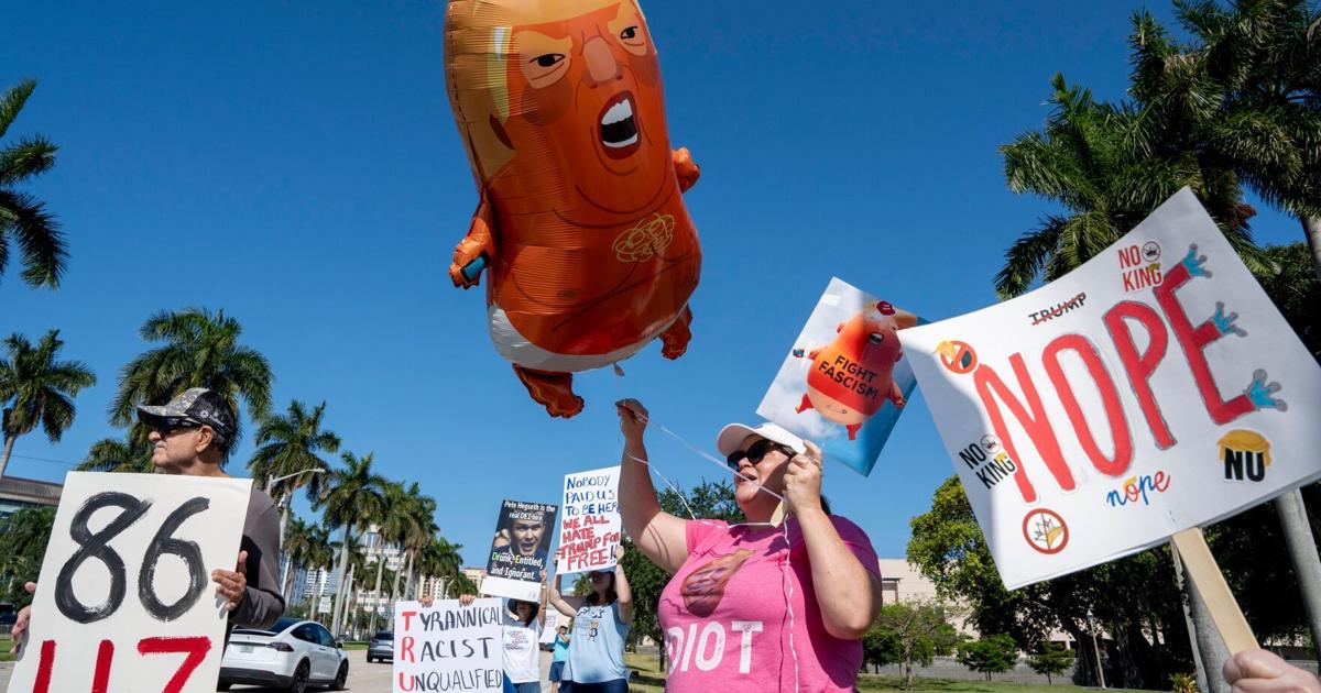 Sarah Anderson holds a sign and balloon as she protests against President Donald Trump before he speaks to the Forum Club of the