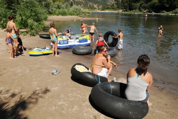 A group of people and assortment of tubes sit on the Clark Fork River bank.