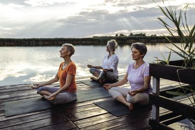 Group of senior woman doing yoga exercises by the lake.