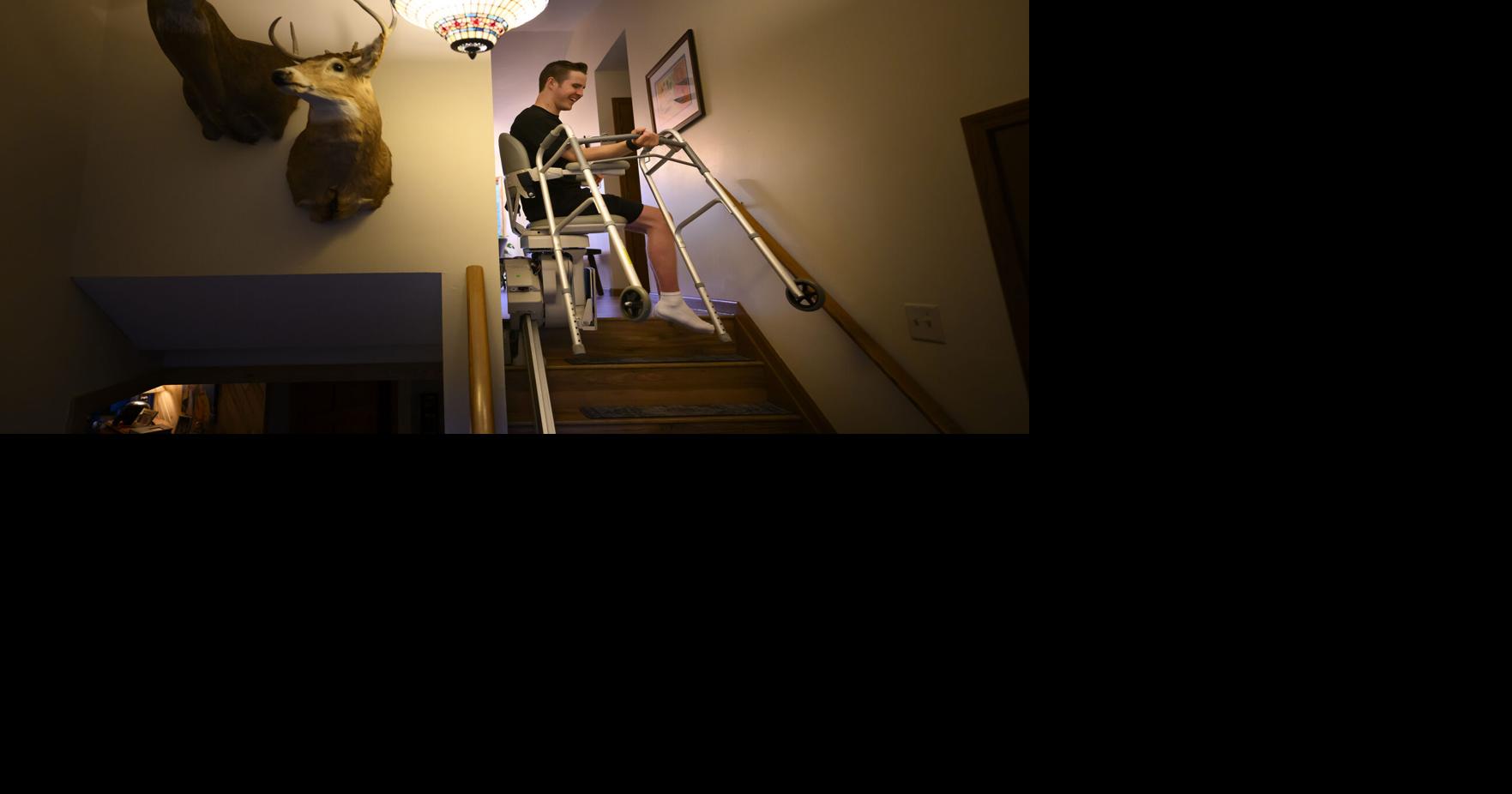 Mason Branstrator carries his walker while using a stair lift to go upstairs for dinner with his parents Tuesday, Aug. 18, 2026, in Duluth, Minn..