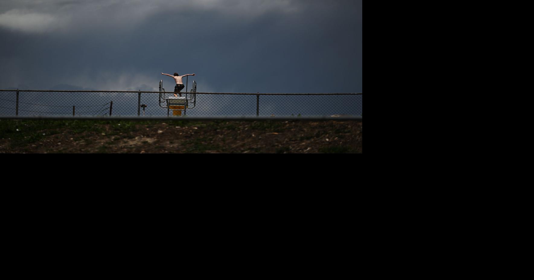 A boy jumps from a diving board at Green Mountain Swim Club as dark clouds move into the area from the west on June 2, 2026, in Lakewood, Colorado.