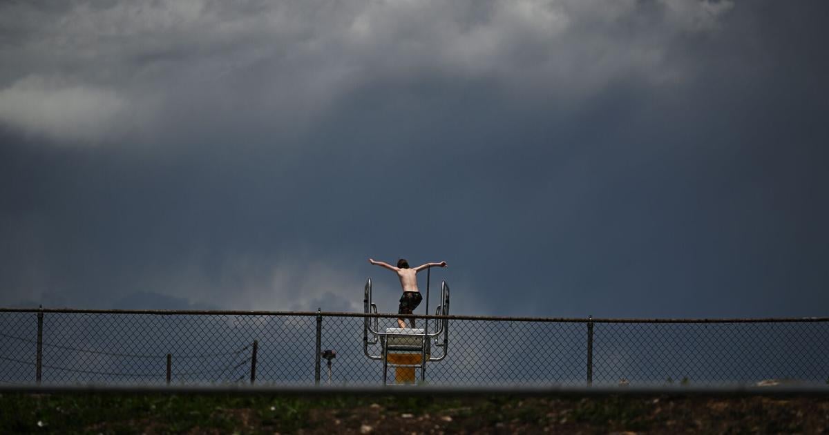 A boy jumps from a diving board at Green Mountain Swim Club as dark clouds move into the area from the west on June 2, 2026, in Lakewood, Colorado.