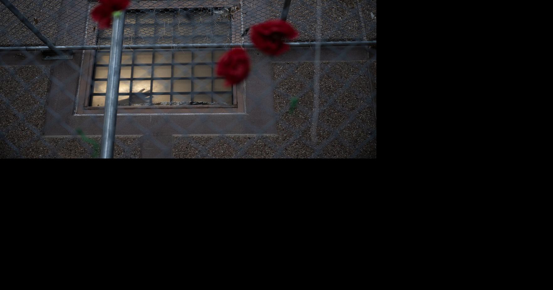 Red poppies are hung on the fence as a detainee places their hands against a window of the Aurora ICE Processing Center during a Passover Grief Vigil on April 8, 2026, in Aurora, Colorado.