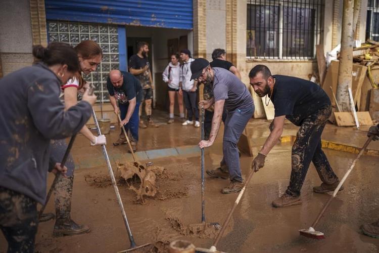 Mud-caked volunteers clean flood debris in a Spanish town as authorities struggle to respond