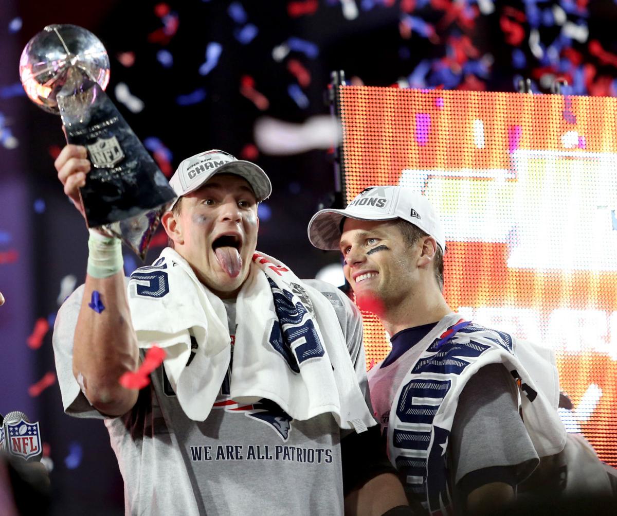 New England Patriots Rob Gronkowski sticks out his tongue as he celebrates with the trophy as Tom Brady looks on.