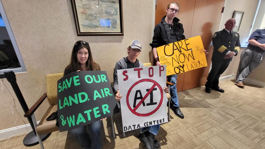 Three people hold anti-AI signs at the Burke commissioners meeting