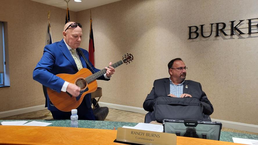 Commissioner Mike Stroud strums a medley of tunes before the meeting