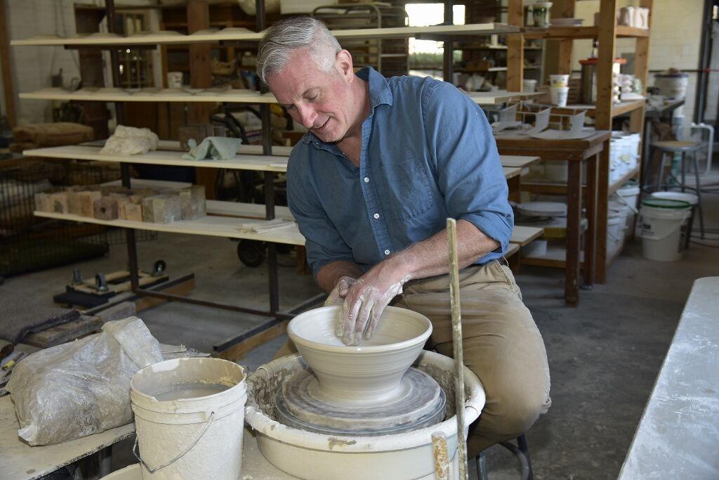 A potter, Hamilton Williams, throwing a bowl on a potter's wheel with a cluttered studio in the background.
