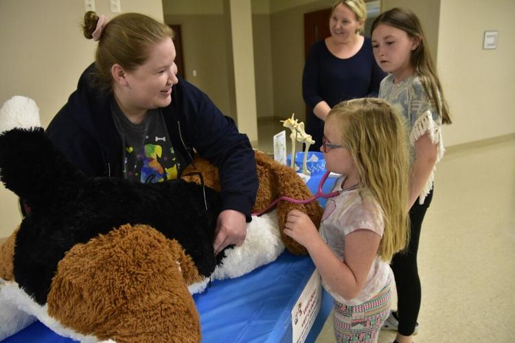 Veterinarian Dr. Jennifer McGrady from Animal Hospital of East Burke shows Willow Scott how vets conduct animal exams using a stuff dog. Also pictured are mom Angie Scott and Julia Scott (center). the family graduated from the CVHF program.