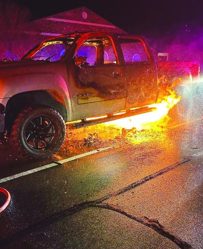 The remains of a pickup truck after a fire, with firemen observing the damage.
