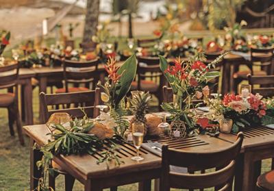 Wooden tables for wedding dinner decorated with tropical flowers, pineapples, coconuts and glass lamps. View of the ocean. Concept of a tropical destination wedding.