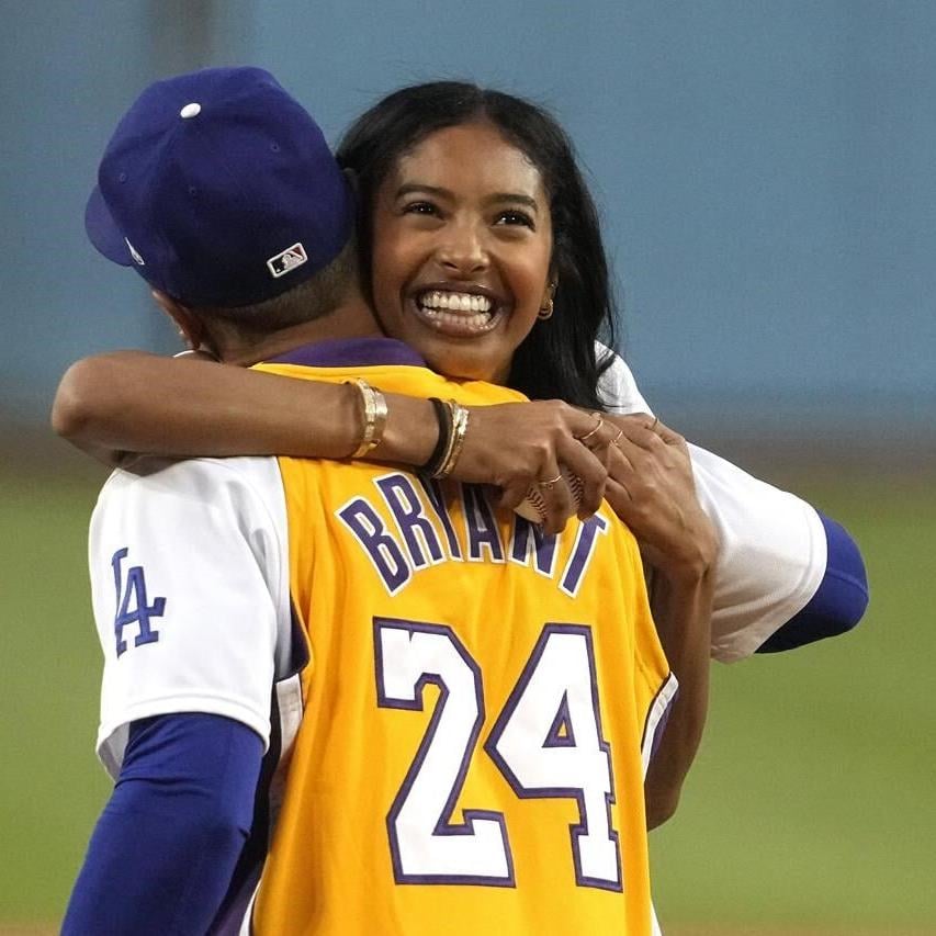 Vanessa Bryant, right, widow of Kobe Bryant, hugs Los Angeles Dodgers'  Mookie Betts as Dodgers co-owner Stan Kasten looks on prior a baseball game  between the Dodgers and the Atlanta Braves Friday