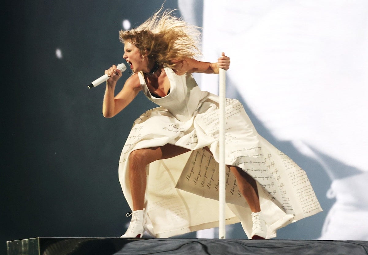 Swift wears a white dress with cursive writing on it and appears to be screaming.