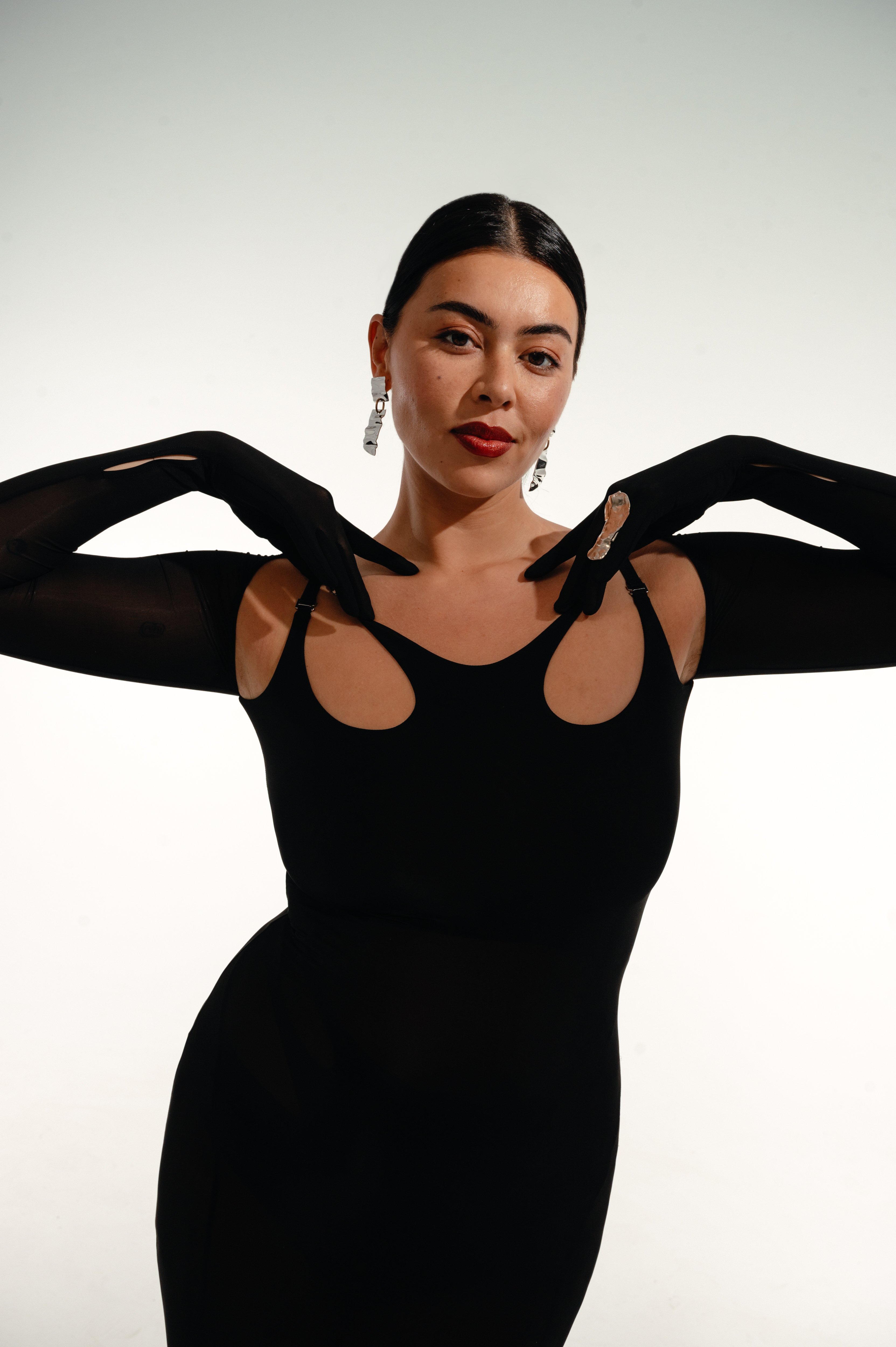 A portrait of Lauren Chan, who is wearing a black Dion Lee dress, Giuseppe Zanotti shoes, and Michelle Ross earrings and ring.